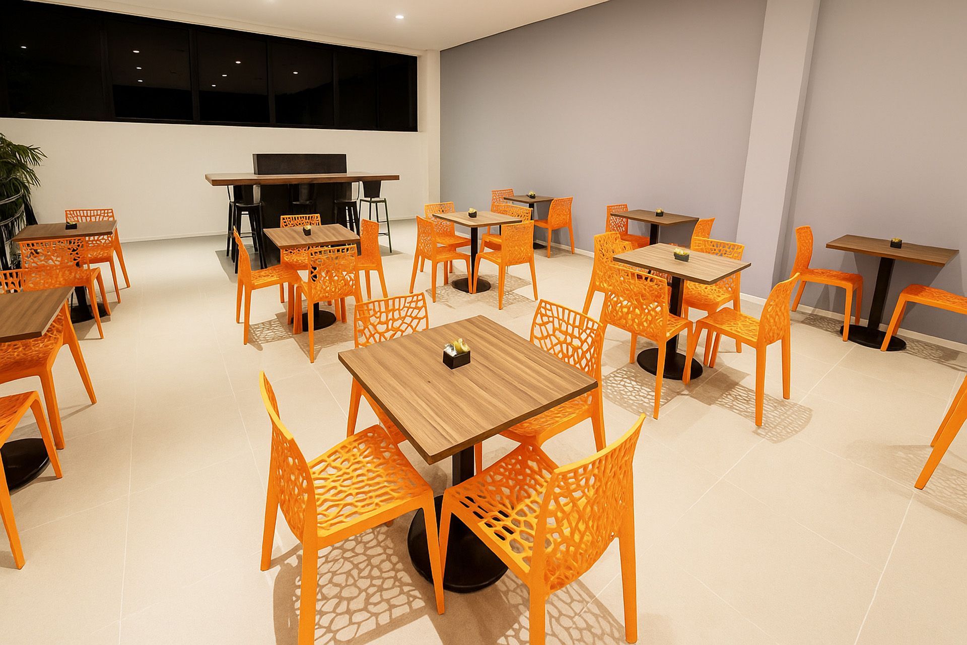 Interior de restaurante com cadeiras laranja, mesas de madeira e bar preto.