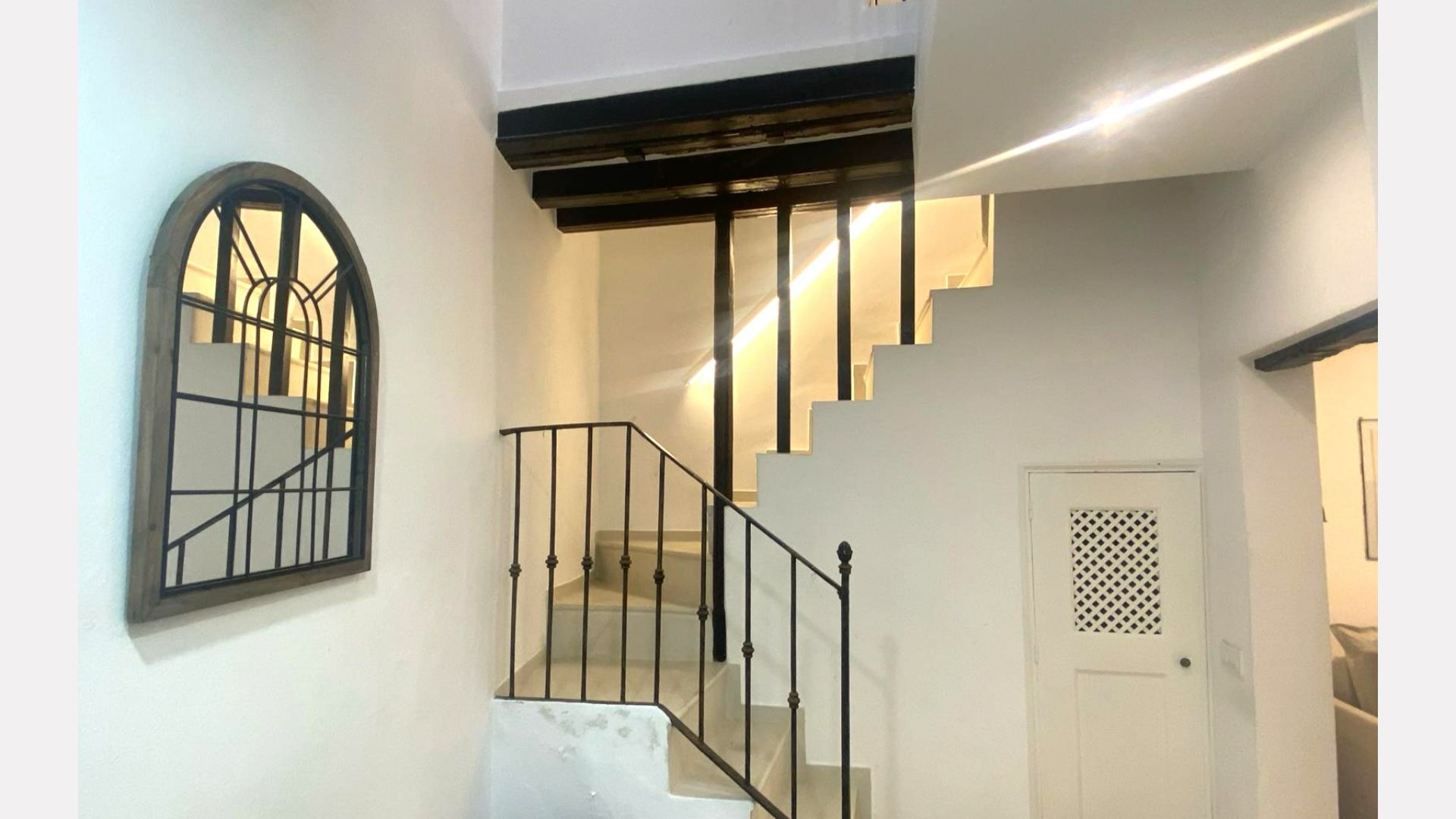 Staircase with black railing and wooden beams. A mirror hangs on the wall, and there's a white door.