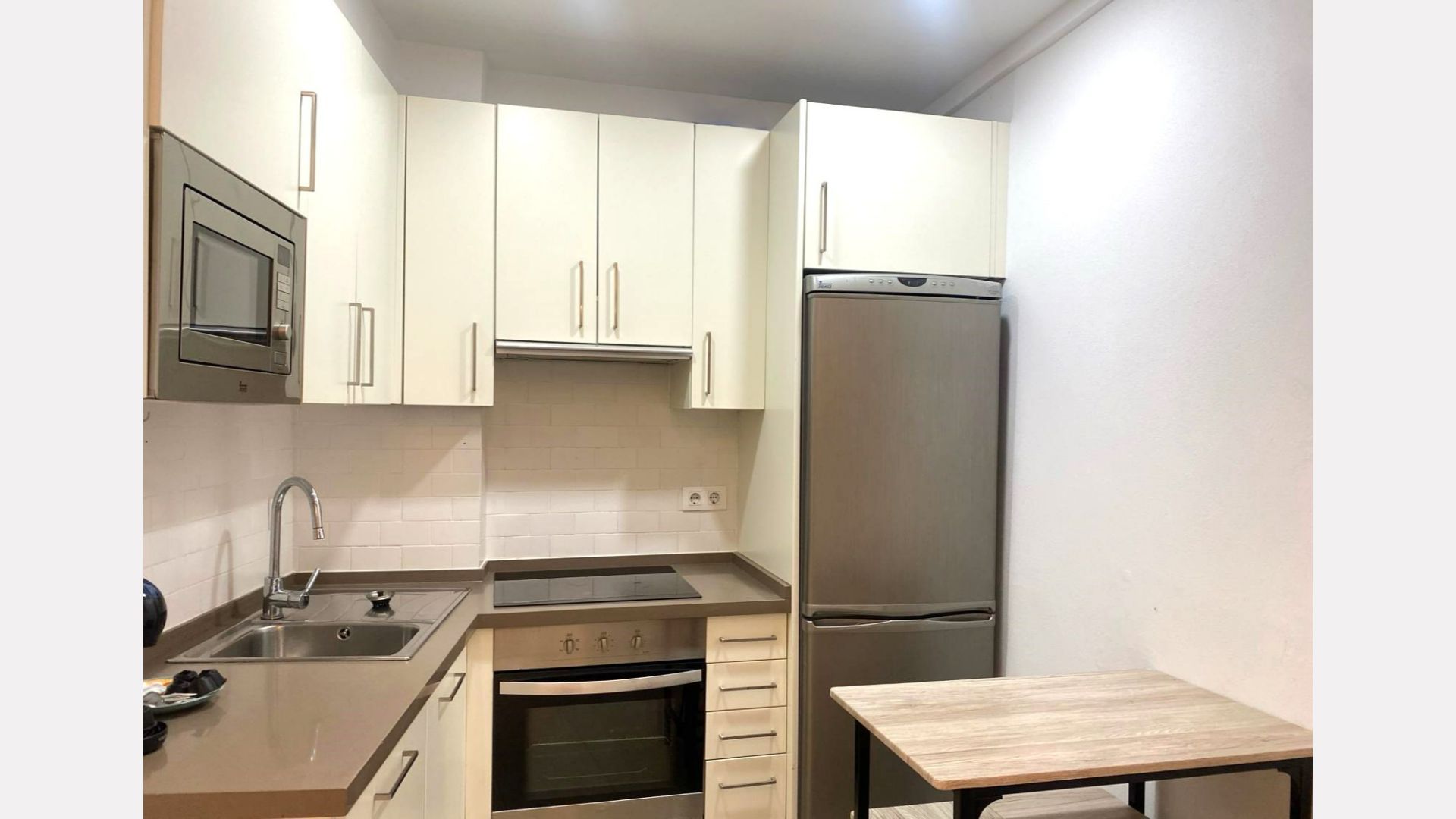 Small kitchen with white cabinets, stainless steel appliances, and a small table.