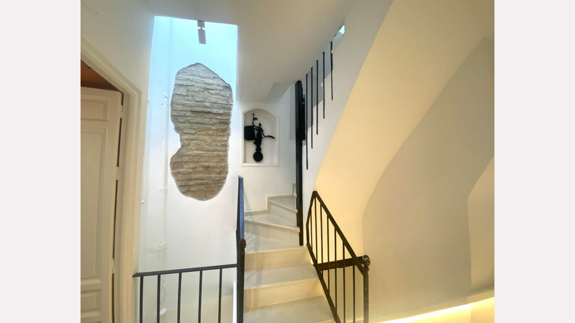 Staircase with marble steps, white walls, and a section of exposed brick. Black metal railings.