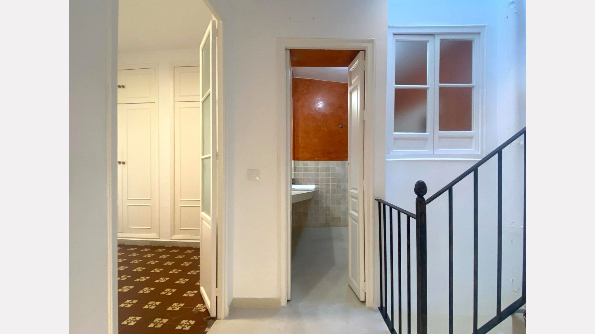 Hallway with doors to rooms and a bathroom, next to a staircase with a window.
