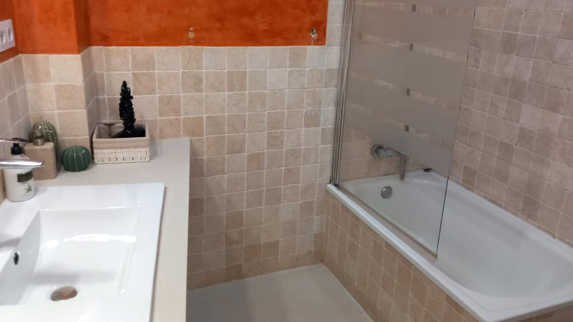 Bathroom with white sink, bathtub, and tan tile walls. Orange accent wall.