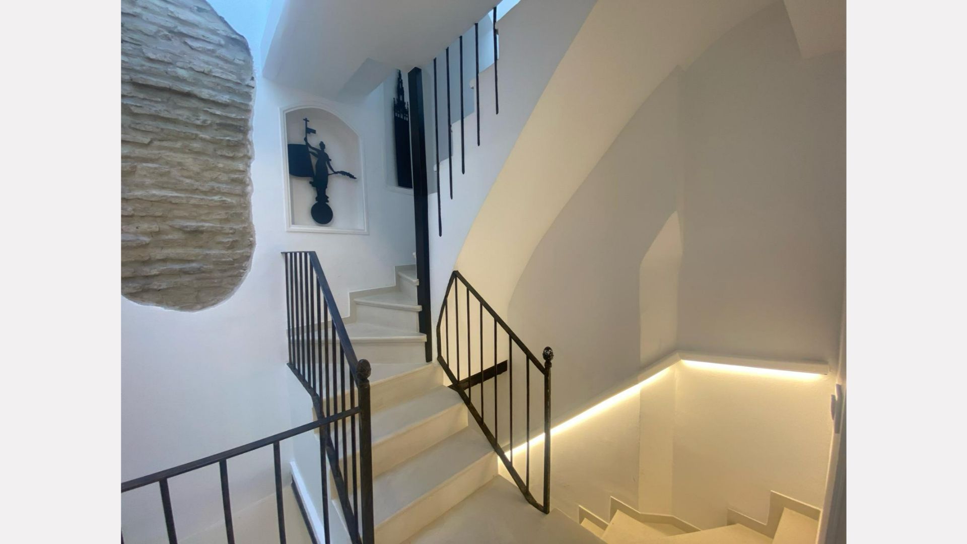 Staircase with white walls, black railing, and built-in lighting. Art hangs on the wall.