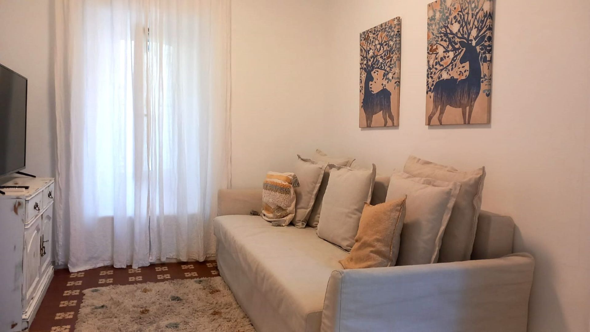 Living room with beige sofa, pillows, two deer art pieces, window with curtains.