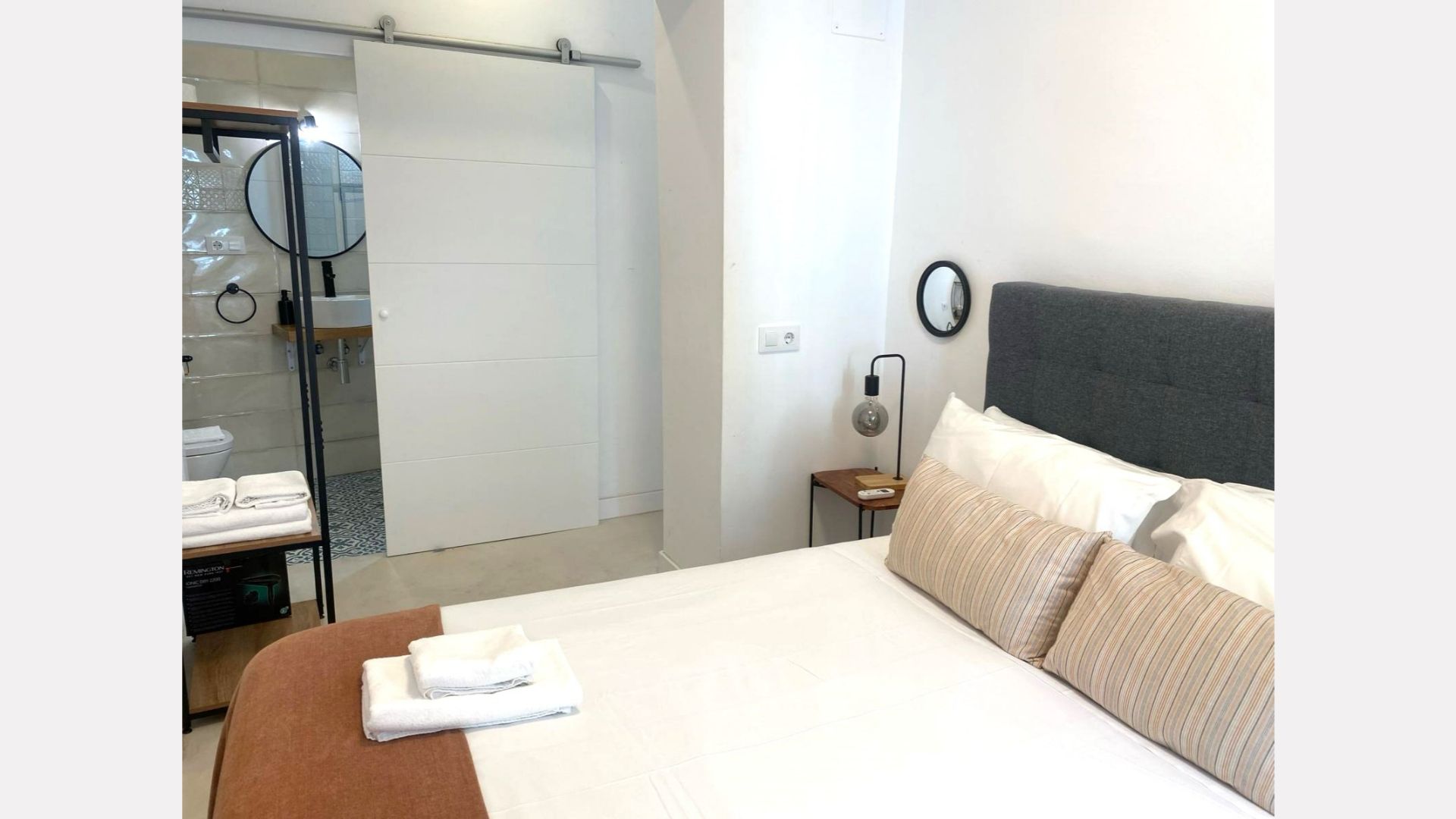 Bedroom with bed, bathroom behind sliding door, neutral colors.