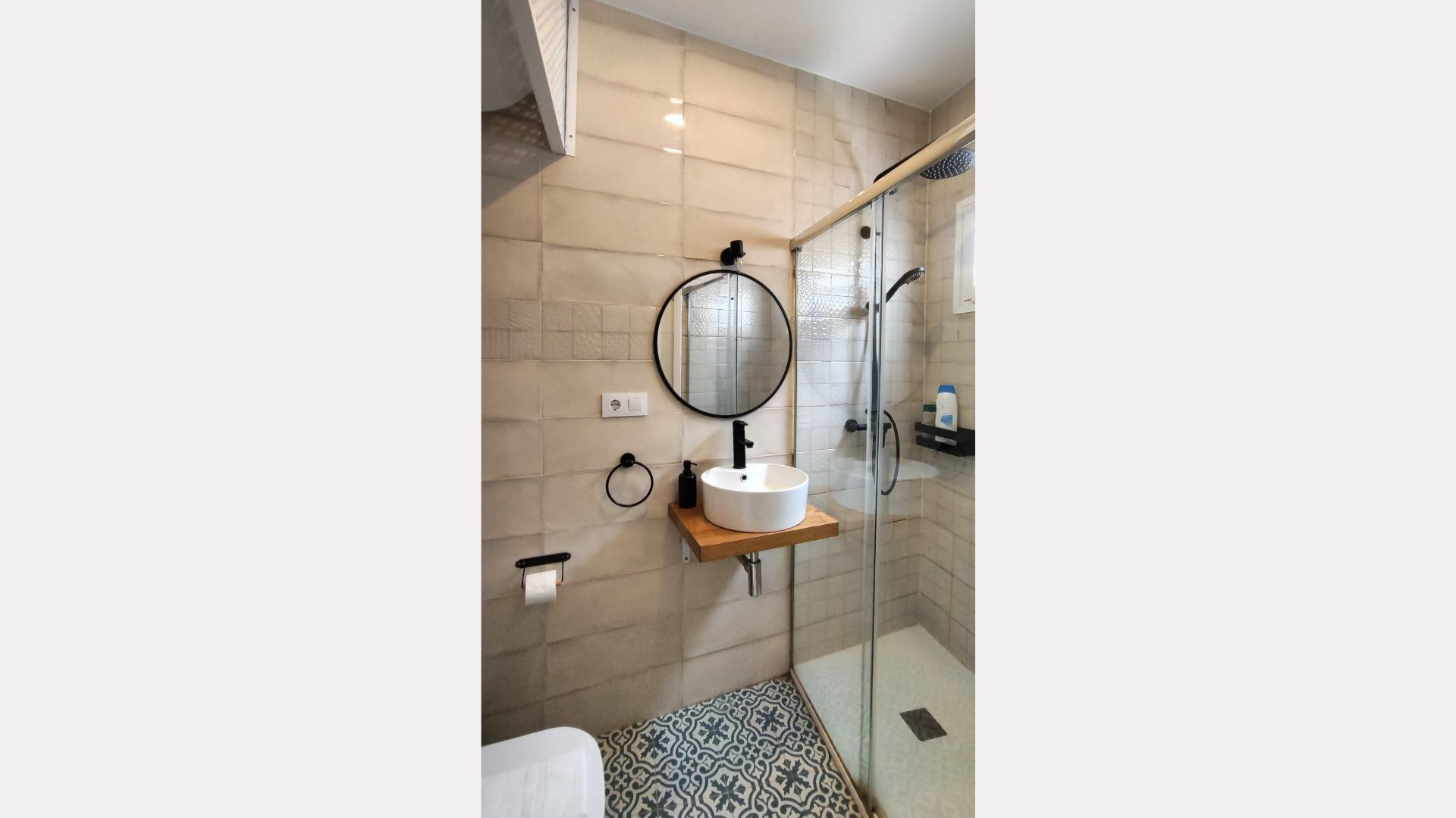 Small modern bathroom with shower, sink, and toilet; neutral color scheme, black fixtures.