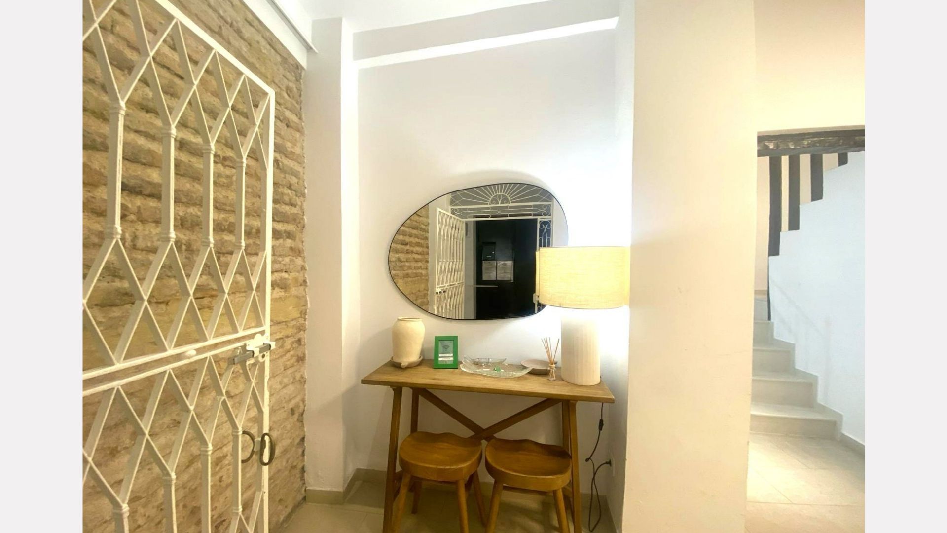 Entryway with mirror, table, stools, brick wall, and decorative metal gate.