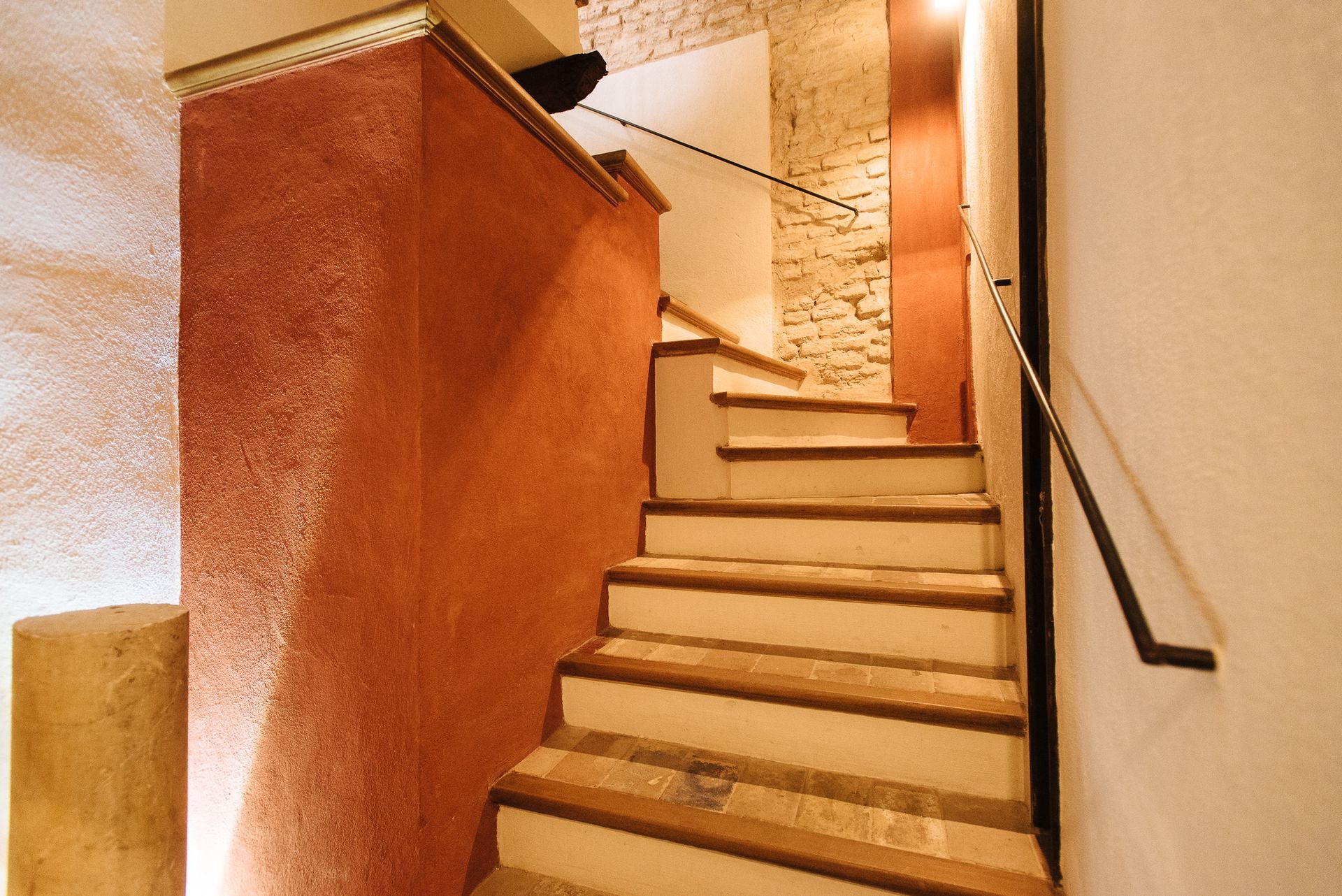 Staircase with reddish-orange wall on the left, leading up. Handrail on the right.