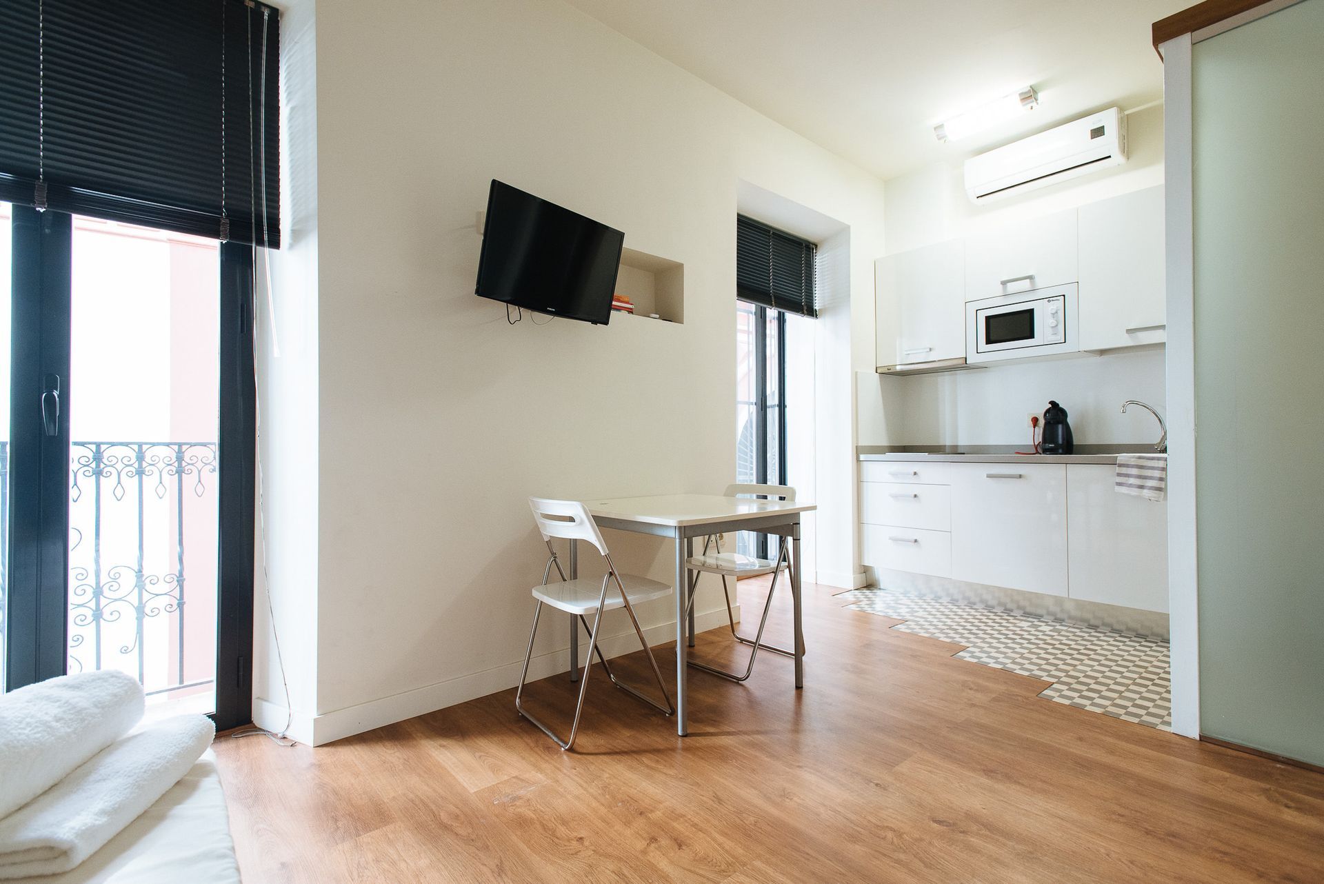 Small apartment interior with kitchen, table, chairs, TV, and balcony.