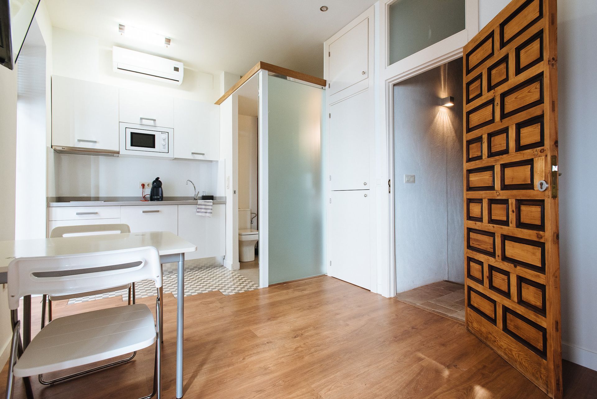 Small apartment interior with kitchen, dining area, and decorative wooden door.