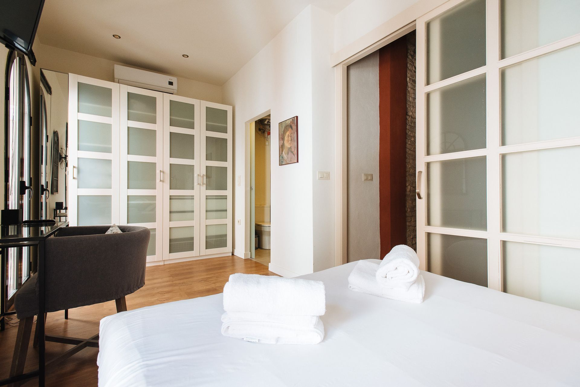 Bedroom with white bed, closet, sliding glass door, and chair.