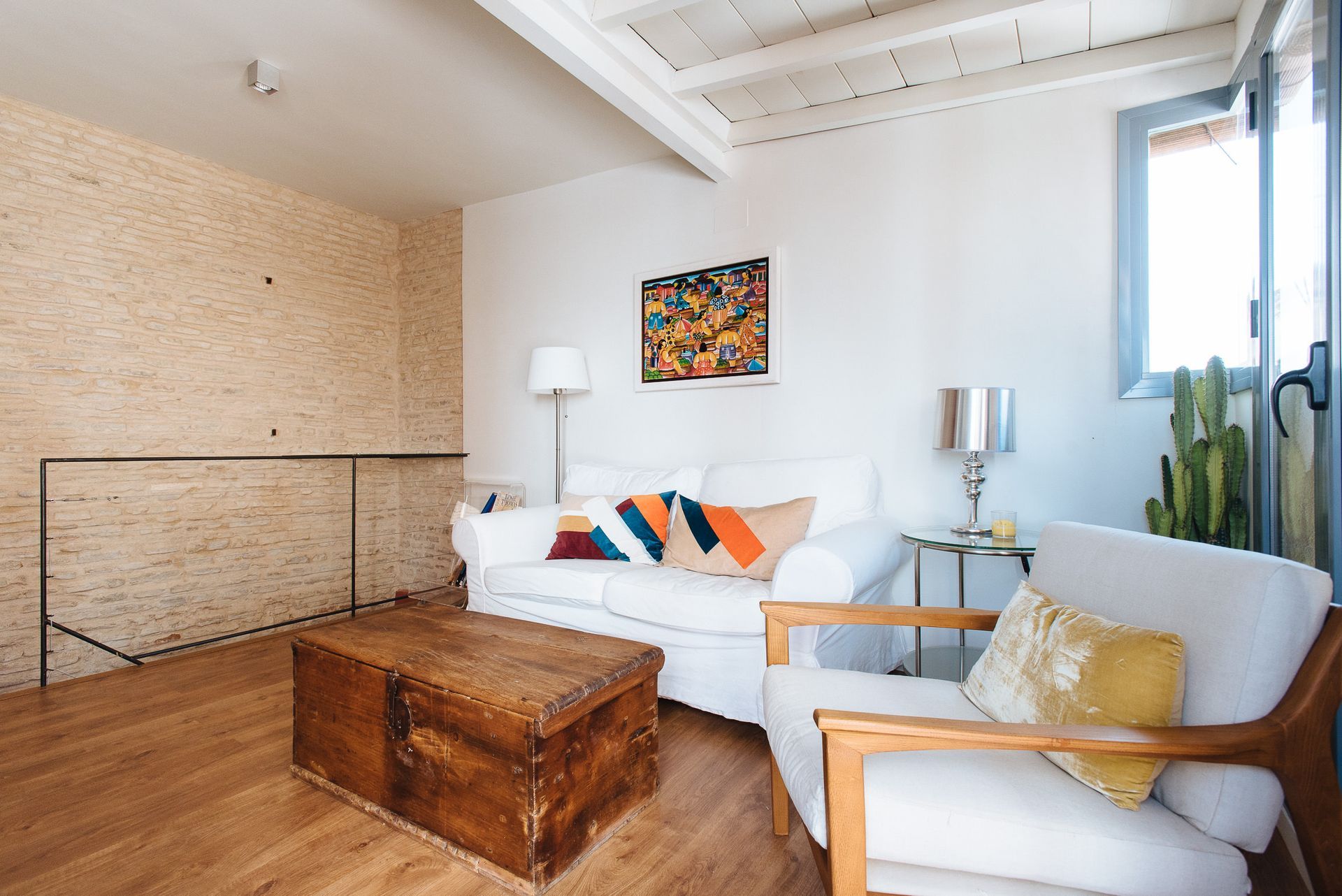 Living room with white sofa, wooden furniture, artwork, and a cactus.