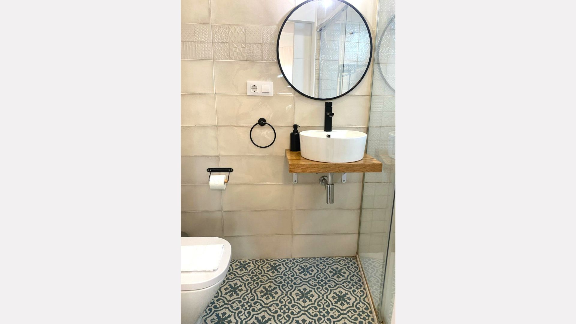 Modern bathroom with patterned floor tiles, white walls, round mirror, and floating sink.