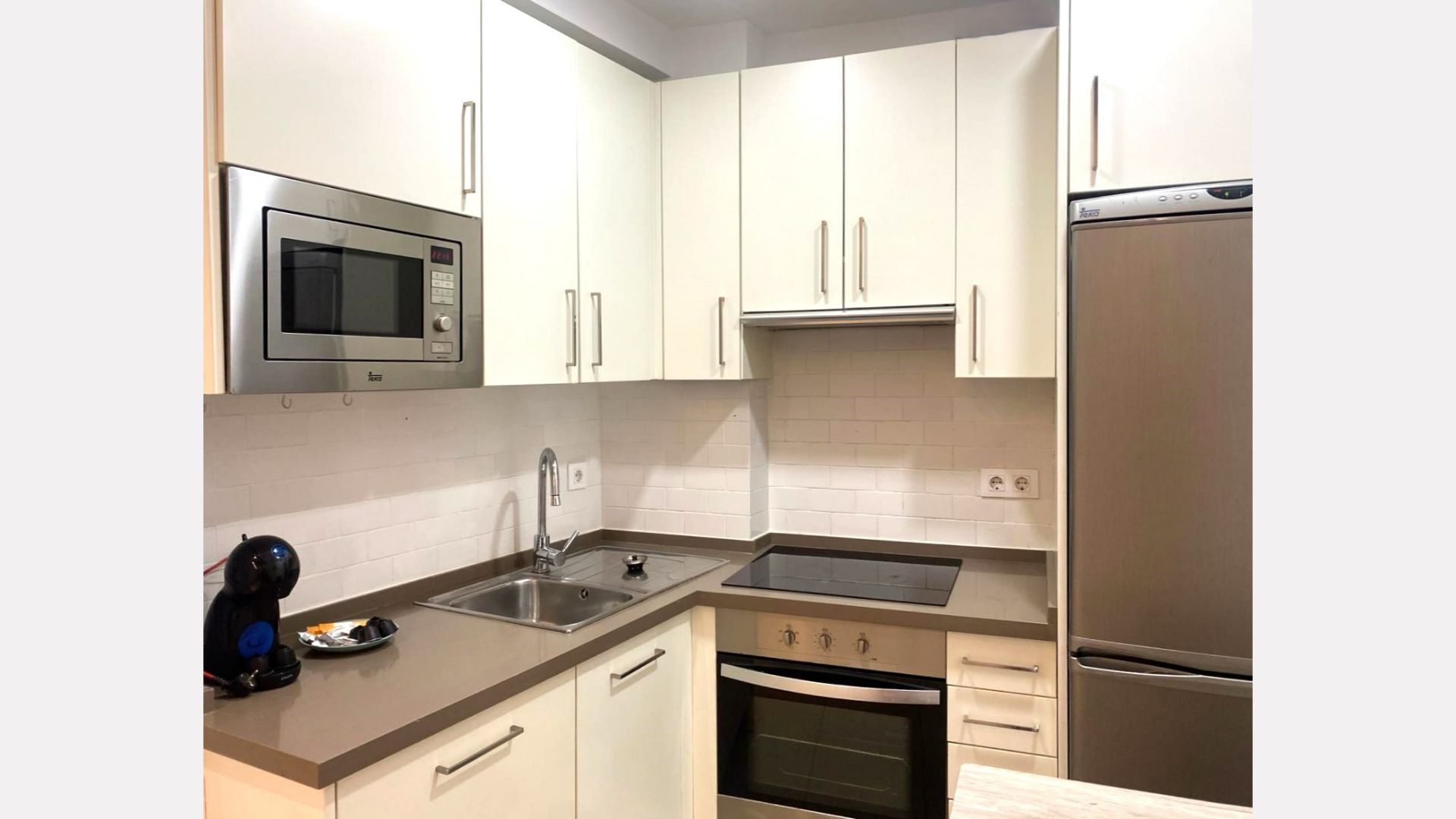 Modern, small kitchen with white cabinets, stainless steel appliances, and gray countertop.