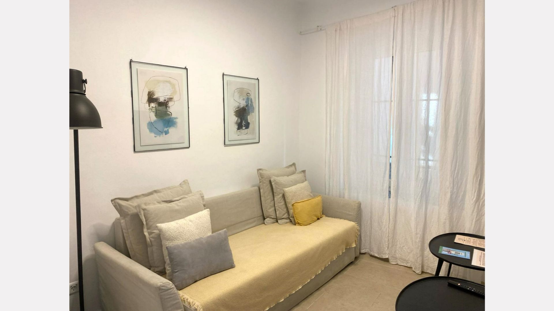 Cozy room with a daybed, pillows, two framed art pieces, sheer white curtains, and a black side table.