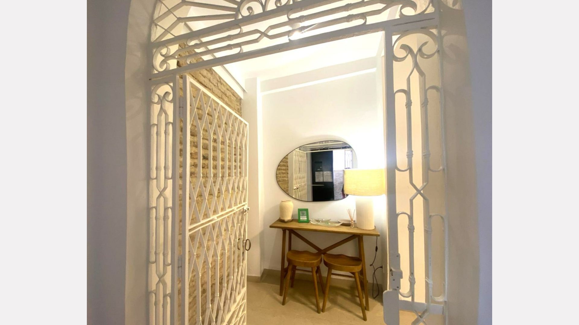 An entryway with white metal gate and a small wooden table with mirror and lamp.