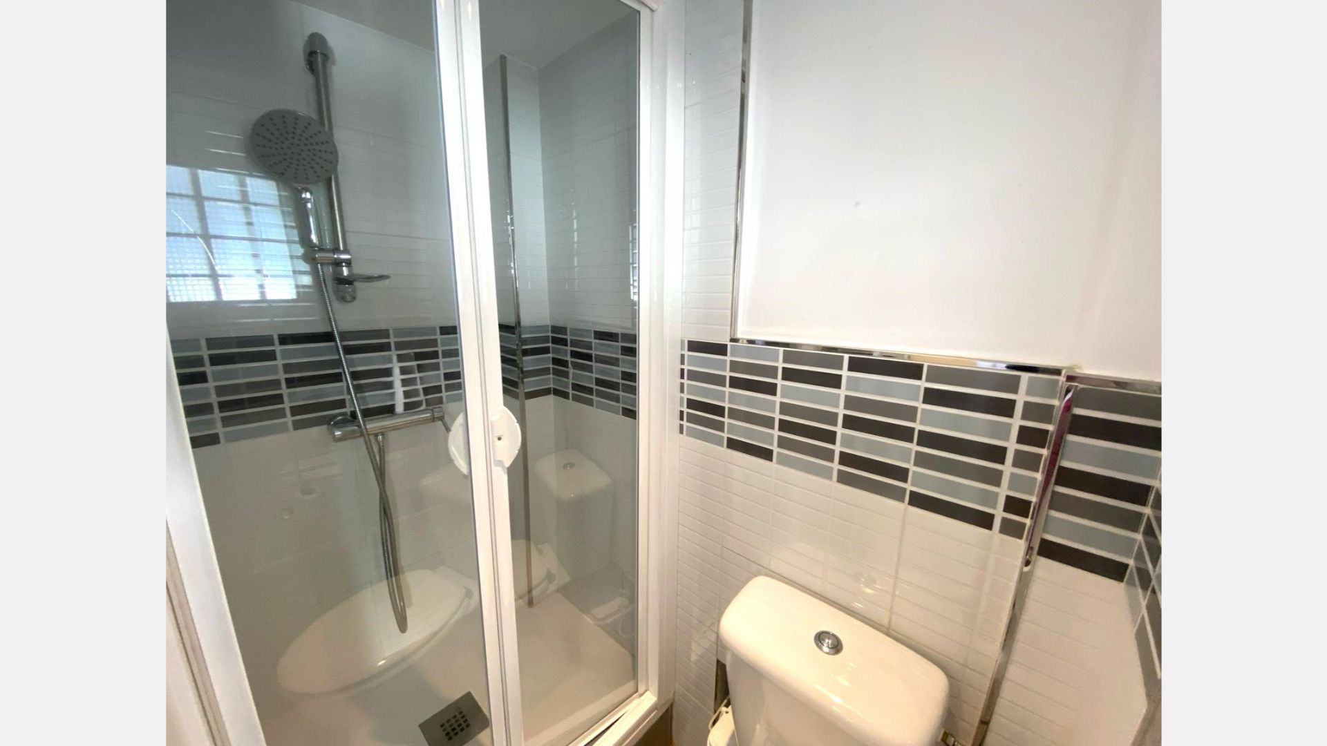 Small bathroom with glass shower, toilet, and mosaic tile backsplash.