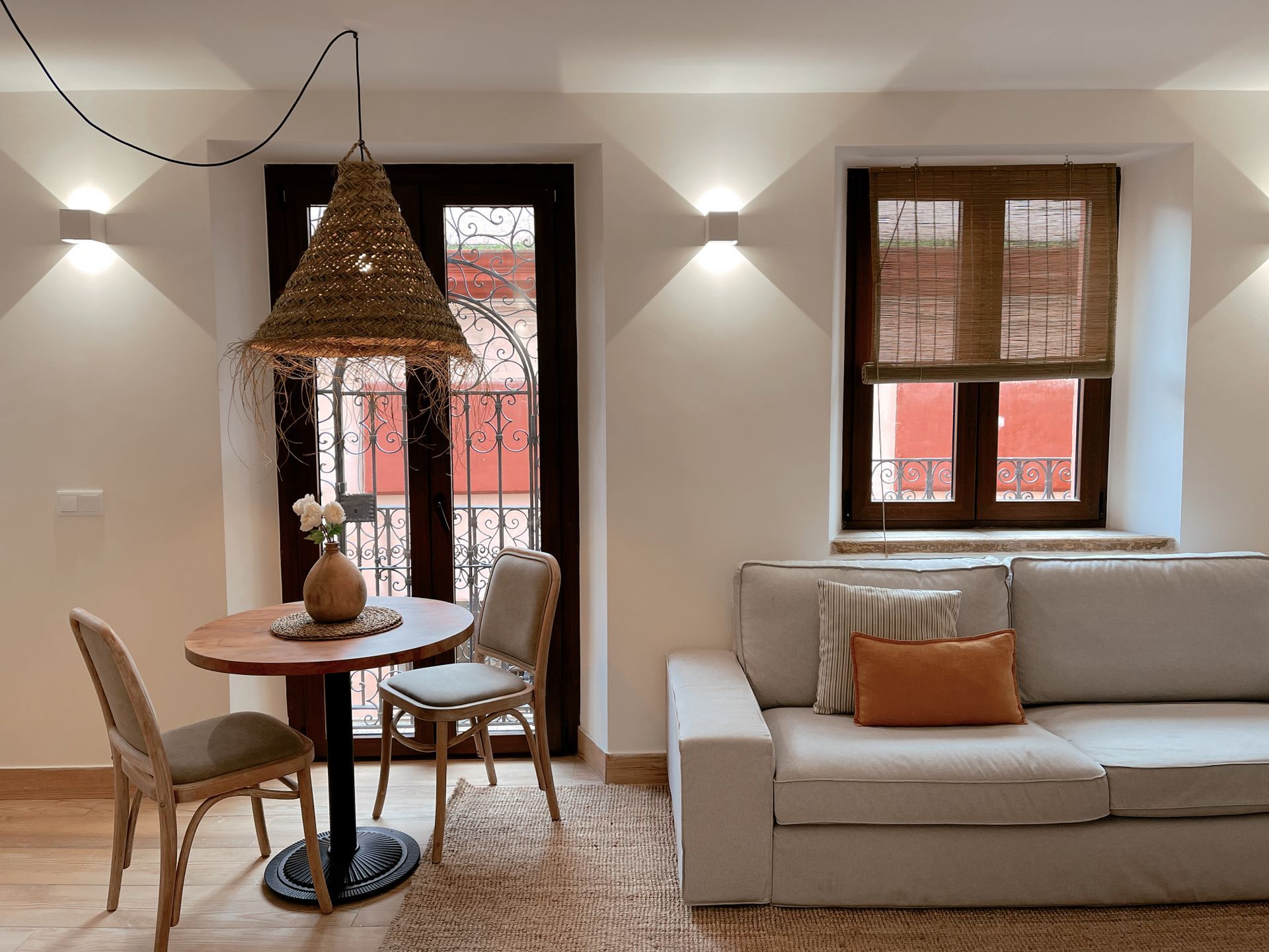 Cozy living space with table, chairs, sofa, windows, and decorative lighting.