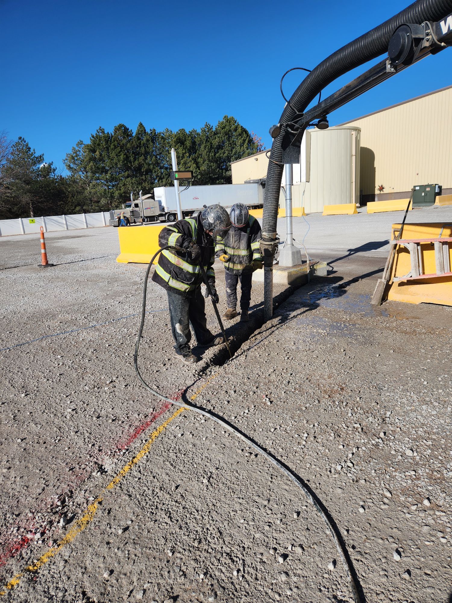 A mobile industrial vacuum unit positioned next to large white storage silos on a gravel lot under a clear blue sky.