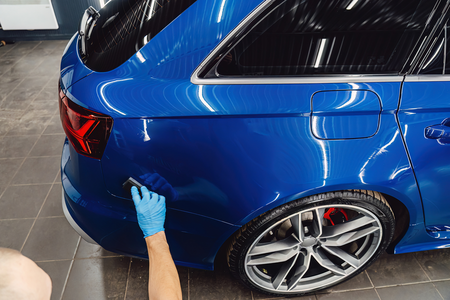 Gloved hand polishing a blue car’s rear quarter panel in a garage