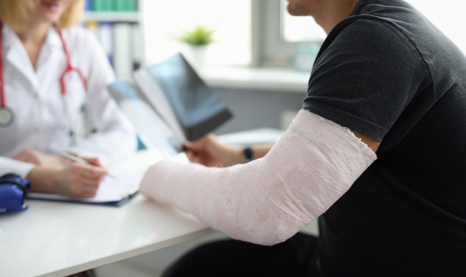 Patient with arm cast talking to doctor in clinic consultation room