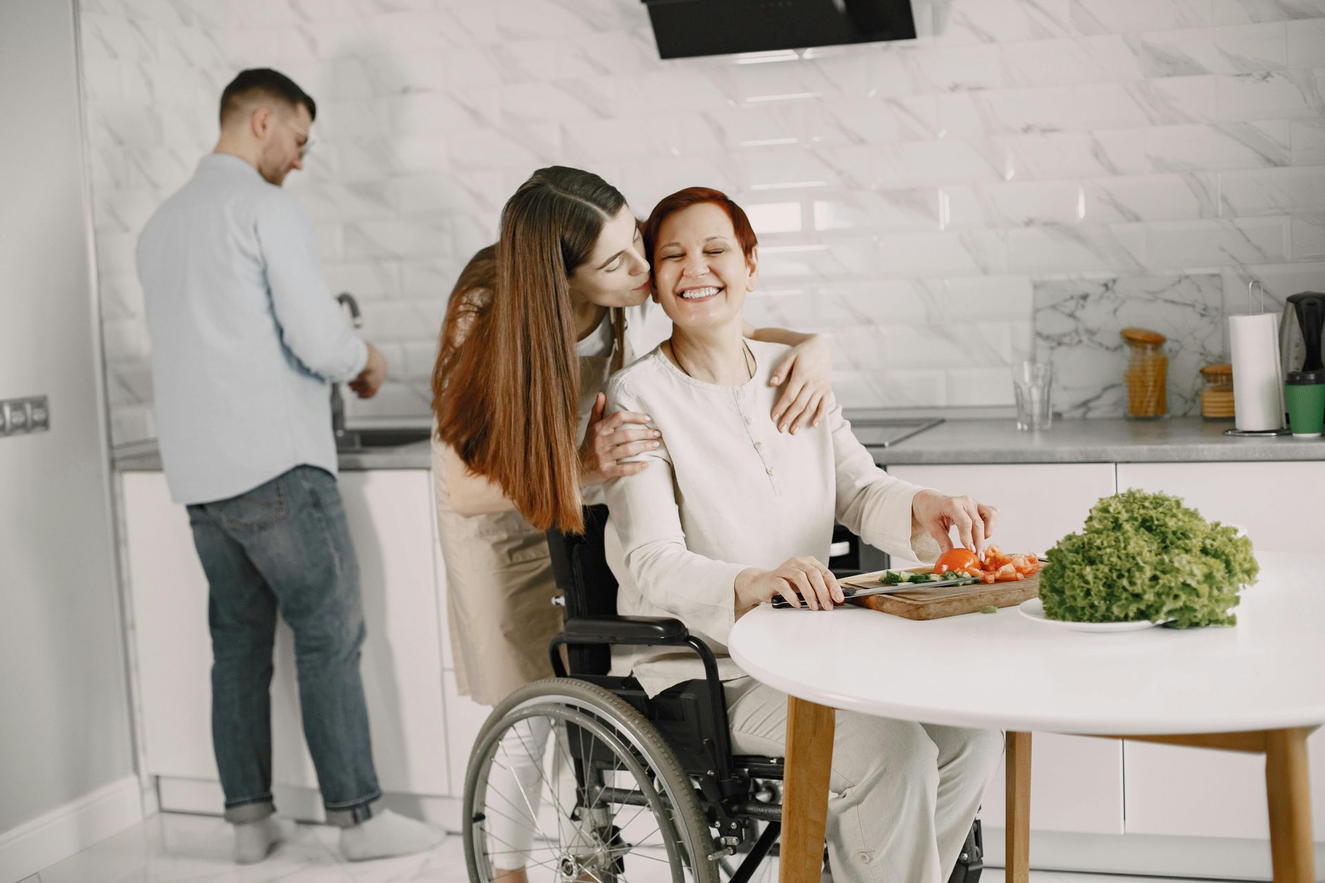 Two women sharing a meal at a table, one in a wheelchair, in a bright kitchen.