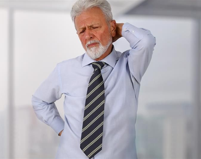 Man in office setting, holding his back and neck, showing signs of pain. Man in office setting, holding his back and neck, showing signs of pain.