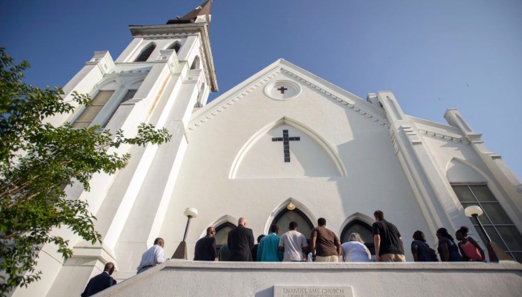 Mother Emanuel with a cross above the entrance; people gathered on steps. Blue sky backdrop.