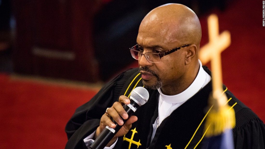 Rev. Manning speaking into a microphone, wearing a robe, in a church.