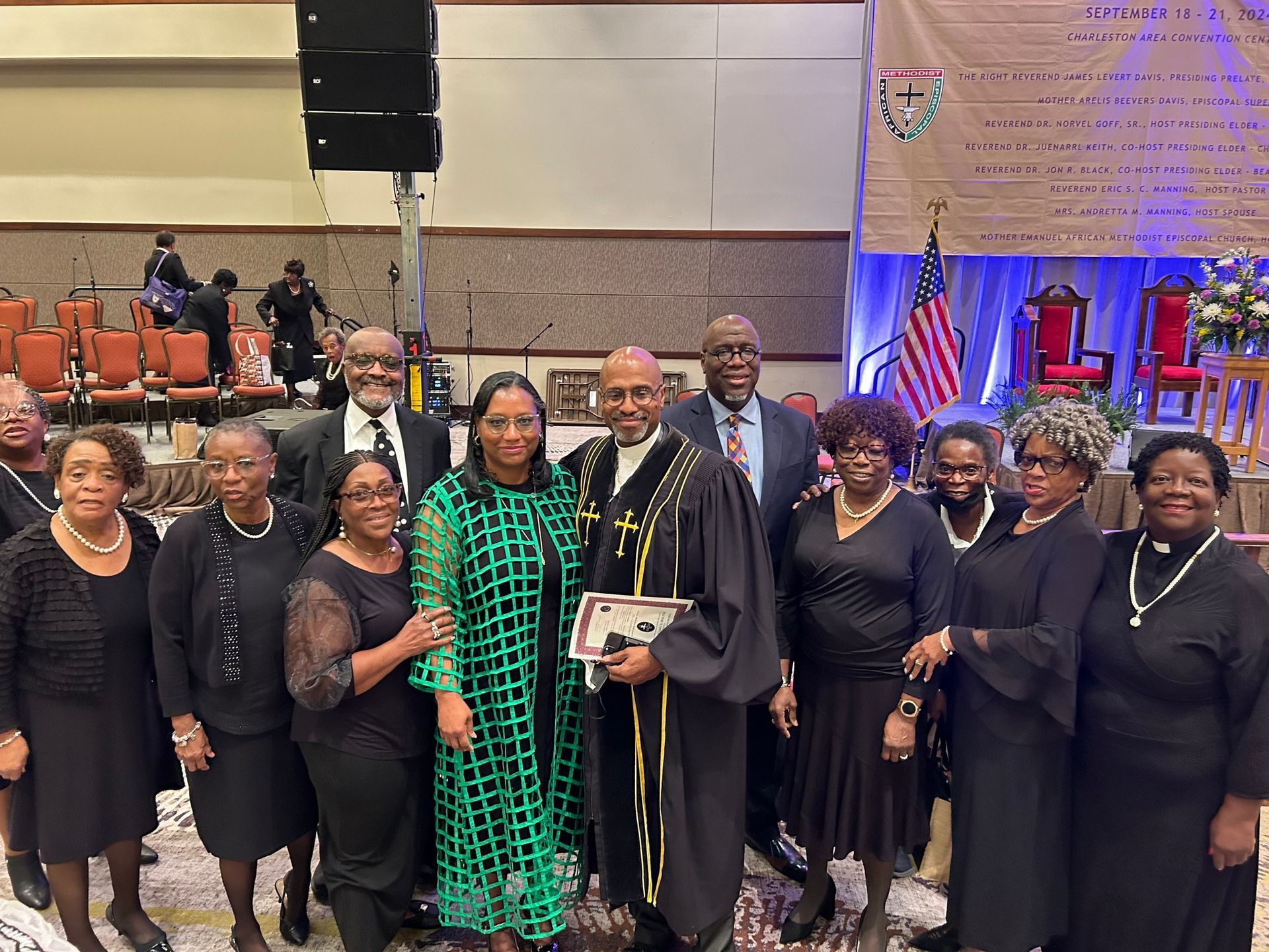 Members of Mother Emanuel poses, formal attire, church setting; Reverend Manning in clerical garb holds is pastoral appointment to Mother Emanuel, smiles.
