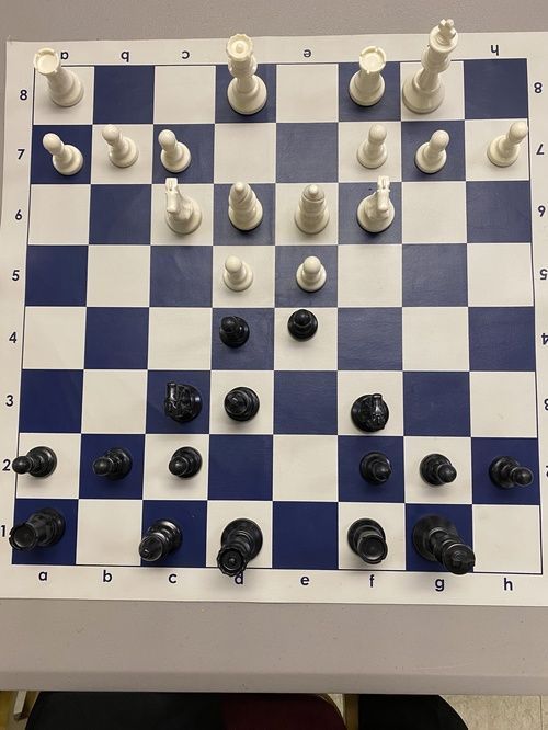 Chessboard with white and black pieces in the middle of a game. Blue and white squares, pieces set up on board.