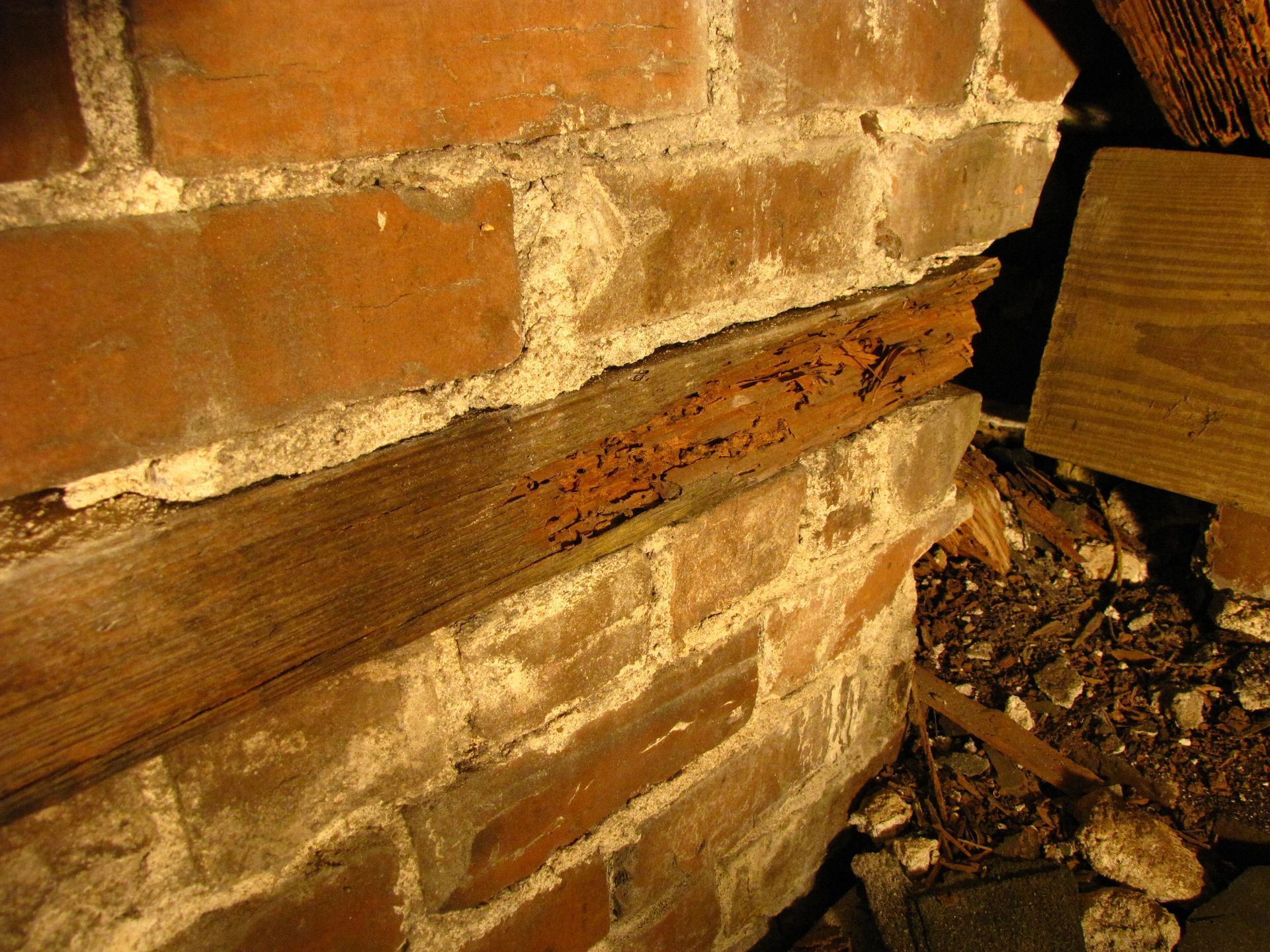 Damaged brick wall with a cracked wooden beam and debris on the floor