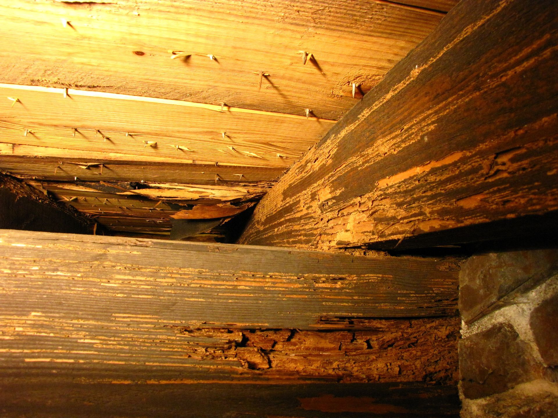 Close-up of dark, weathered wooden beams with visible damage and decay inside a structure