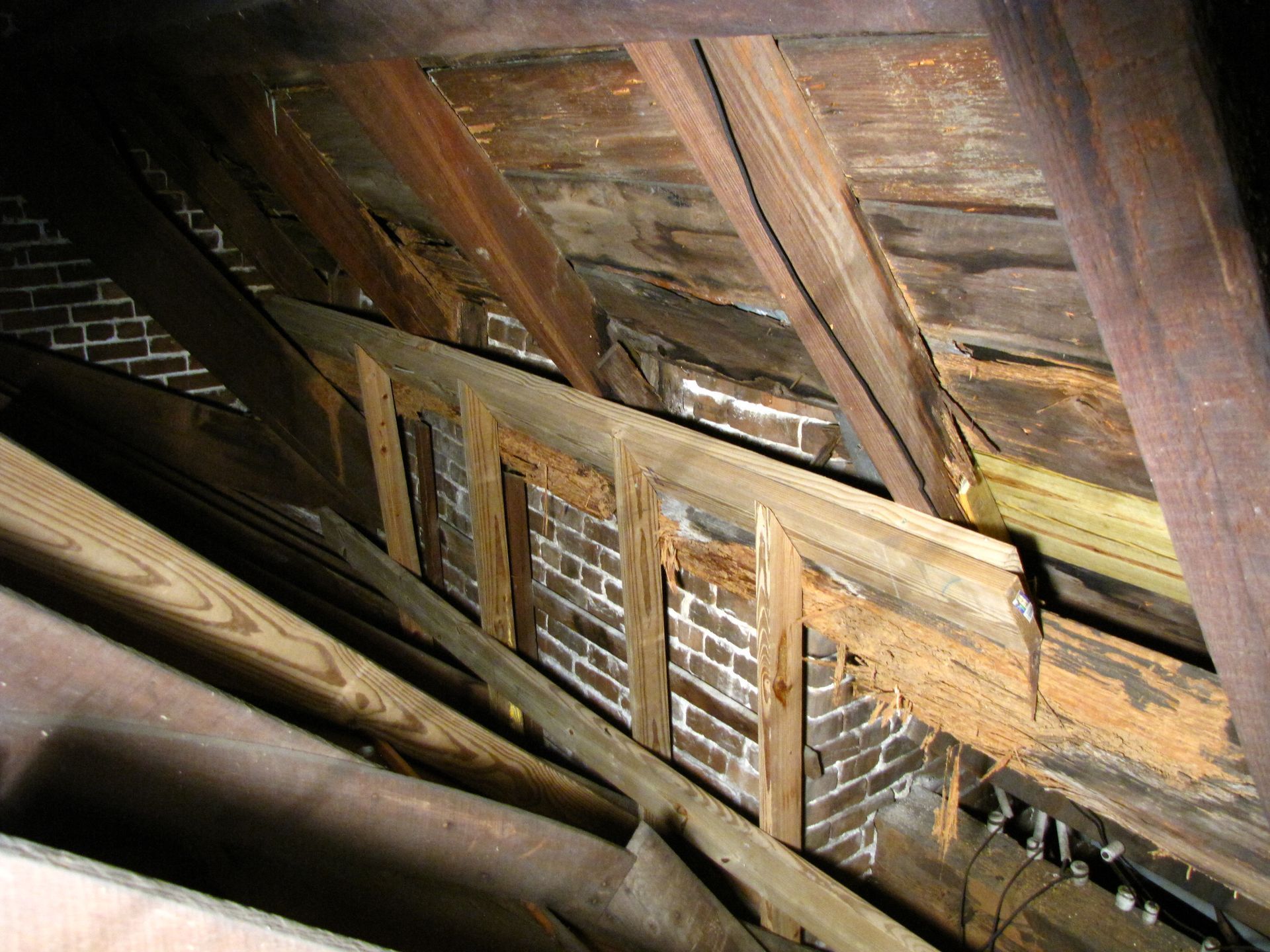 Looking up through a damaged wooden attic roof with exposed beams and weathered boards.