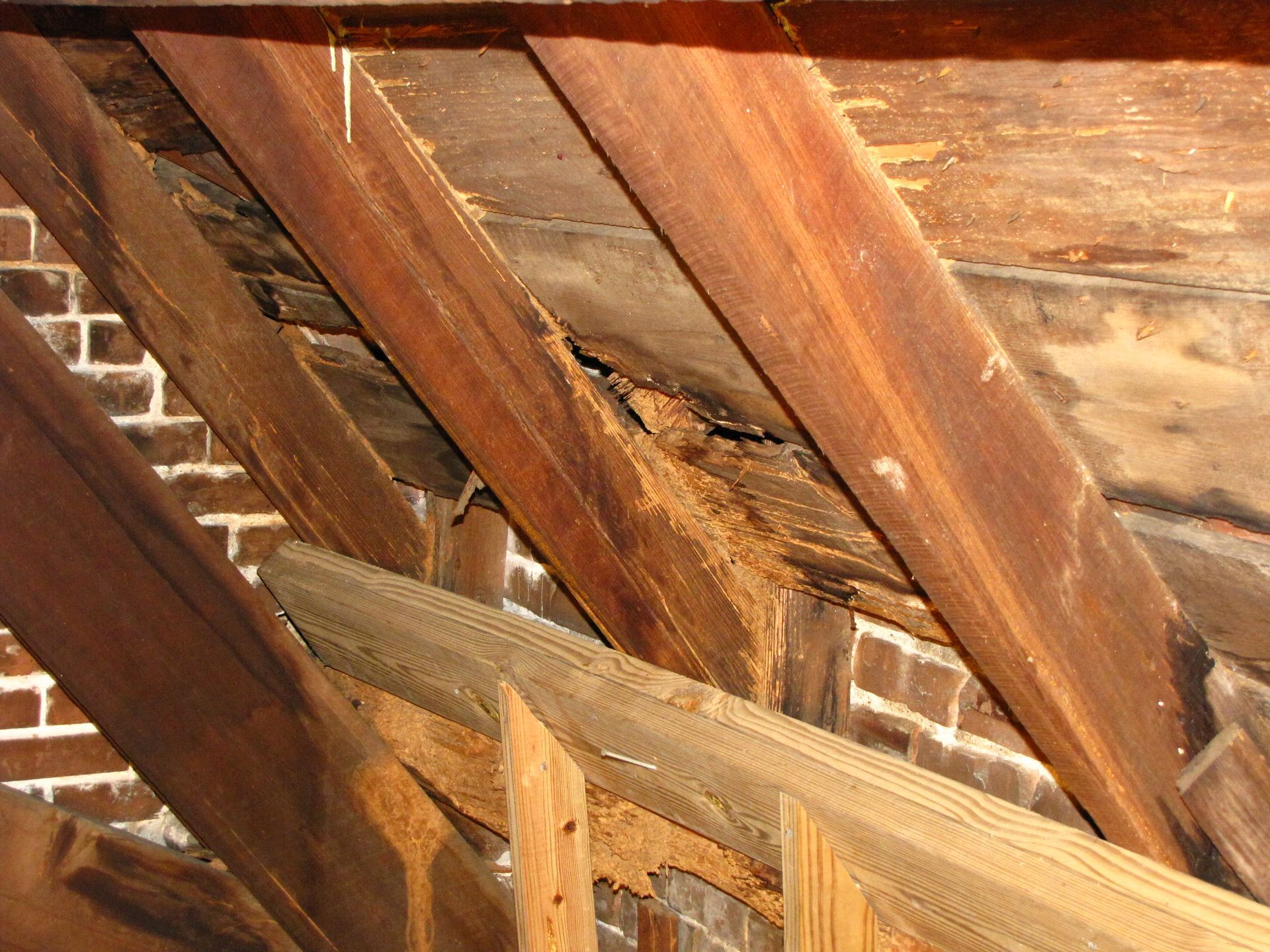 Damaged wooden roof beams with exposed insulation and crumbling plaster indoors