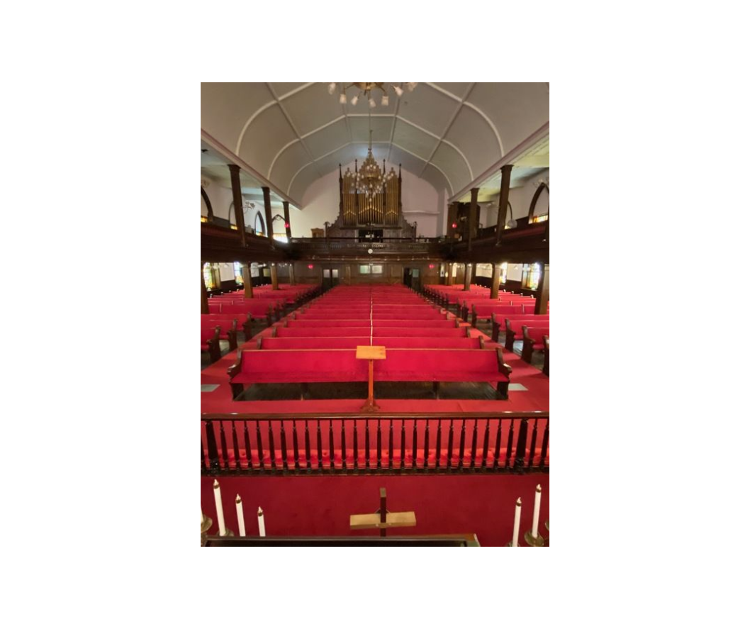 Interior of a church with red pews, carpet, and a wooden altar.