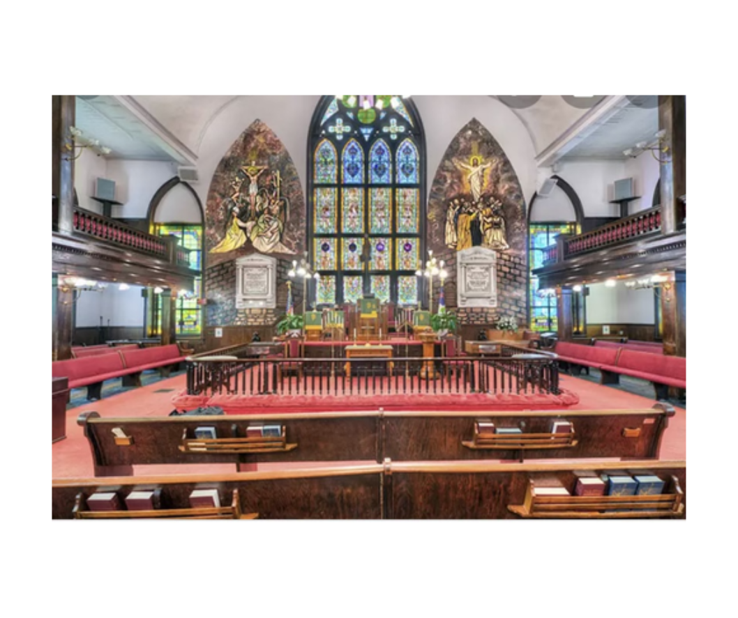 Interior view of a church, with a stained glass window, altar, and rows of pews.