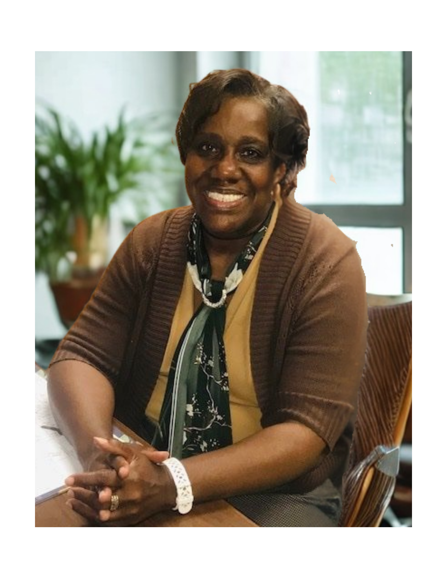 Woman seated smiling at a desk, wearing a brown cardigan and a scarf.