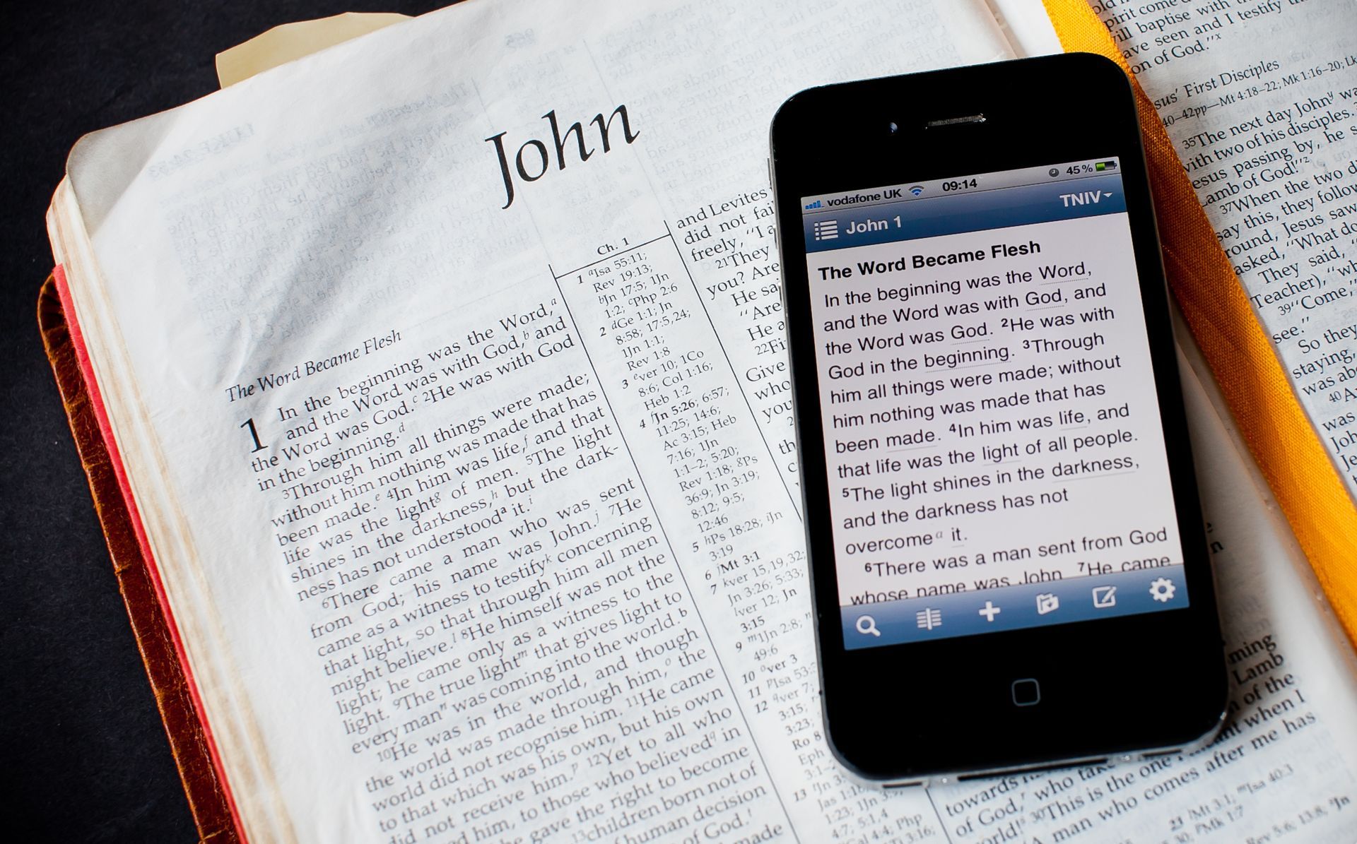 Open Bible next to smartphone displaying text; pencil rests on the page.