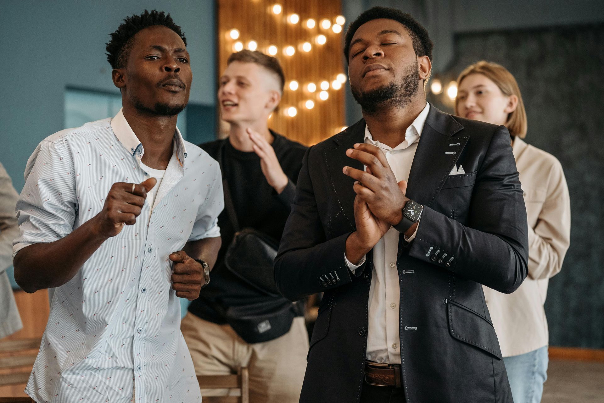 Group of people singing, some with eyes closed, in an indoor setting with warm lighting.