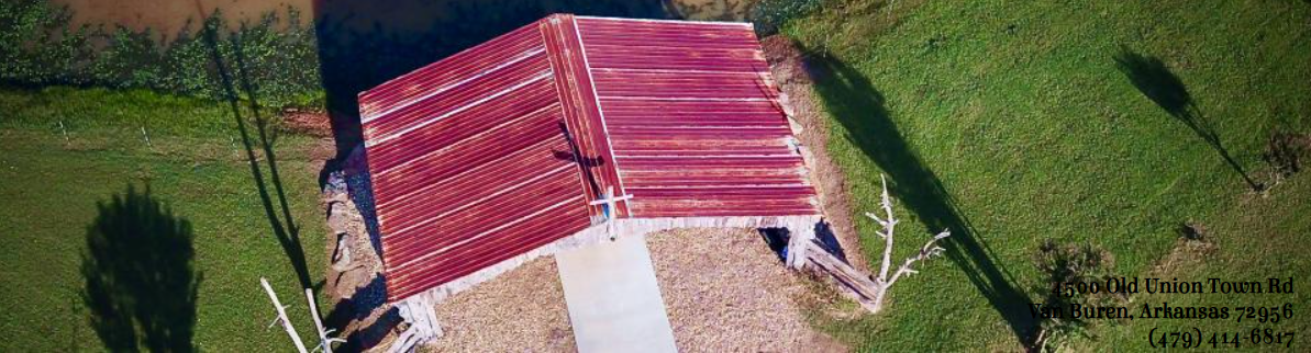 Aerial view of a red-roofed pavilion with a sidewalk, surrounded by green grass and trees.