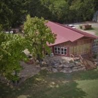 Small cabin with a red roof nestled among trees and rocks beside a grassy yard