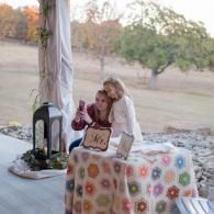 Two people at a decorated outdoor table under a canopy, with a colorful field and trees in the background