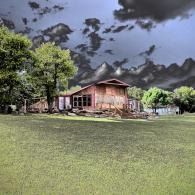 Small wooden cabin with porch in a grassy field under dark storm clouds