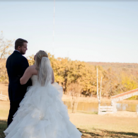 Bride and groom standing together outdoors on a sunny hillside overlooking autumn trees