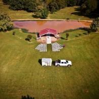 Outdoor wedding setup with chairs and an arch by a pond, with a white truck and trailer on a grassy field