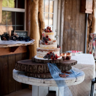 Rustic wedding cake on a wooden table with blue ribbon and desserts in a barn-like setting