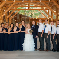 Wedding party posing in a wooden pavilion, bride in white dress with groom and attendants in navy and gray.