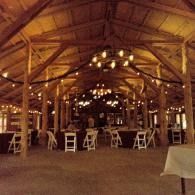 Rustic barn-style event space with warm string lights and white chairs set up for guests