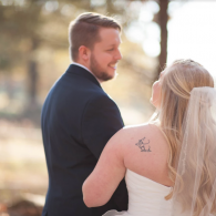 Bride and Groom couple in formal attire smiling outdoors, with the woman facing away in a white dress.
